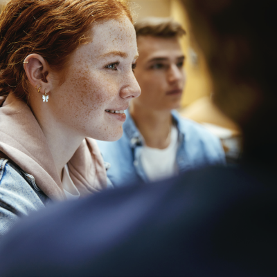 An over-the-shoulder photograph of a ginger-haired, white and freckly woman's smiling expression and profile